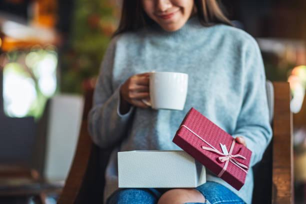 istock a beautiful young woman opening a gift box while drinking coffee 1288756907