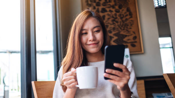 istock a beautiful asian woman holding and using mobile phone while drinking coffee in cafe 1288756920