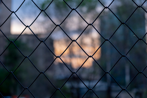 Chain link fence on a blurred city background. Metall wire fence with unfocused city  backgorund.