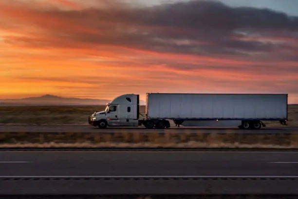 White Semi-Trailer truck speeding down I-70 Interstate under a rural Utah Sunset in the winter time