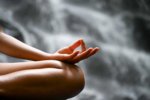 Calm unrecognizable woman meditates in lotus position, sitting in front of waterfall, Nikon Z7
