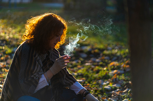 Young woman smoking a cigarette outside. Copy space.