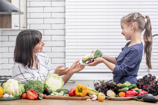 счастливые мама и дочь готовят овощной салат. концепция здорового питания. - mother green sparse contemporary стоковые фото и изображения