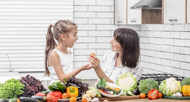 mãe e filha jovens preparando salada vegetal no fundo da cozinha moderna. - mother green sparse contemporary - fotografias e filmes do acervo