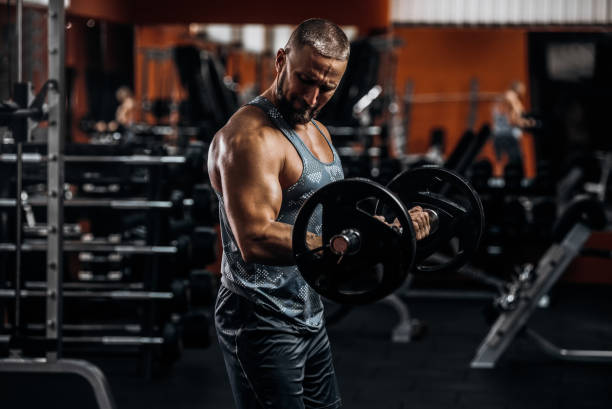 istock Muscular young man lifting weights in gym on dark background 1288786260