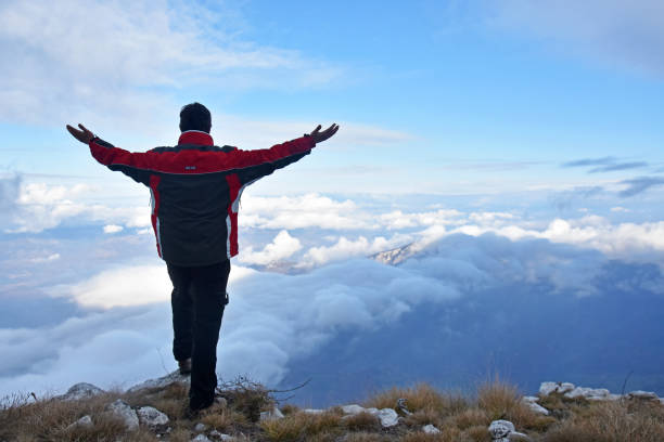 istock Man on cliff rise hands and enjoy looking on a clouds under mountain 1288787338