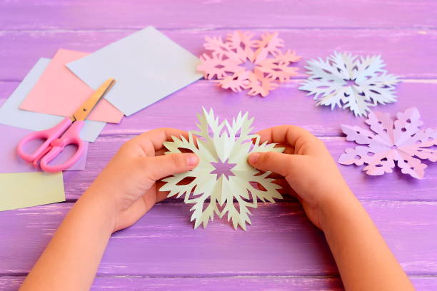 Christmas paper cutouts. Merry Christmas paper craft. Snowflake winter background. Background holiday winter. Christmas cutouts. Christmas cutouts paper snow flake. Christmas cutouts paper craft ideas. Snowflakes background. DIY Christmas cutouts photo. Snow flakes background. Blue snowflake pattern. Snow flake Christmas. Cutting activities for kids scissor practice. Craft supplies for kids el niño tiene un copo de nieve de papel en las manos. papel de color, tijeras, rosa, púrpura, copo de nieve azul en el fondo de madera de vacaciones de invierno. diy navidad escamas de nieve fotos. actividades de corte niños habilidades de tijera en cas
