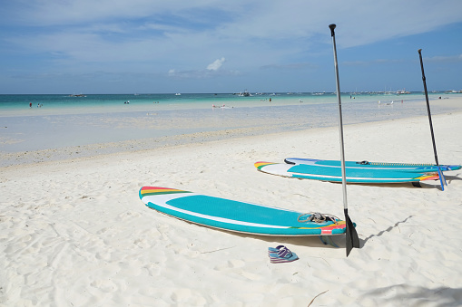 Close up shot of two paddle boards in turquoise color, lying on the clean white sandy beach of Boracay
