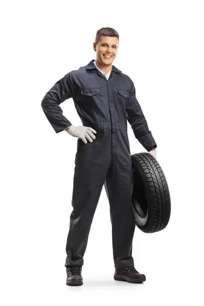 Full length portrait of an auto mechanic worker holding a car tire and smiling isolated on white background