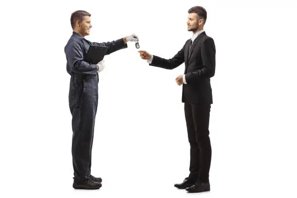 Full length profile shot of worker in a uniform giving car keys to a man in a suit isolated on white background