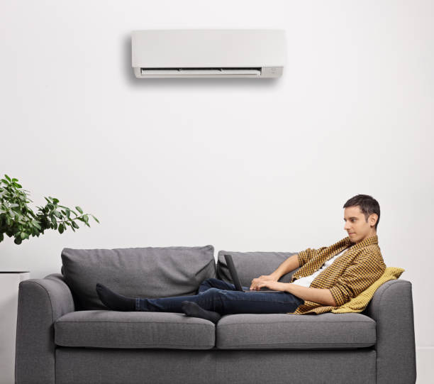 istock Young man working on a laptop and sitting on a sofa under AC unit 1288794766