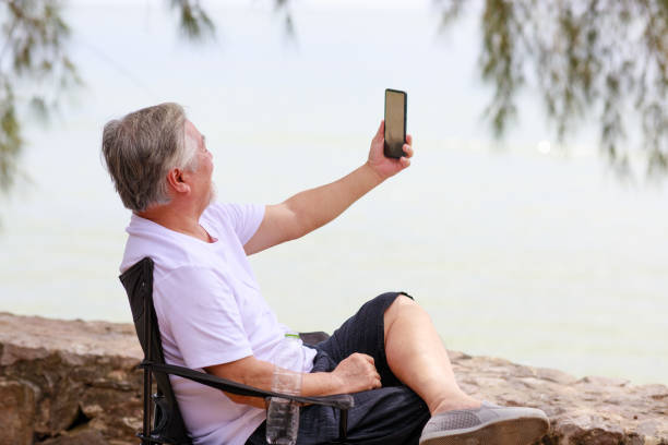 istock Asian senior male using mobile phone for video call communication with his family while vacation next to the beach. 1288796498