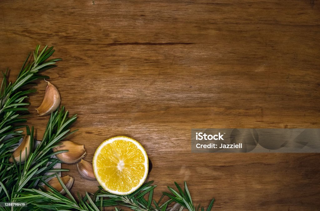 Свежие веточки розмарина, зубчики чеснока и лимонная половина на темной деревянной доске - Стоковые фото Ароматический роялти-фри