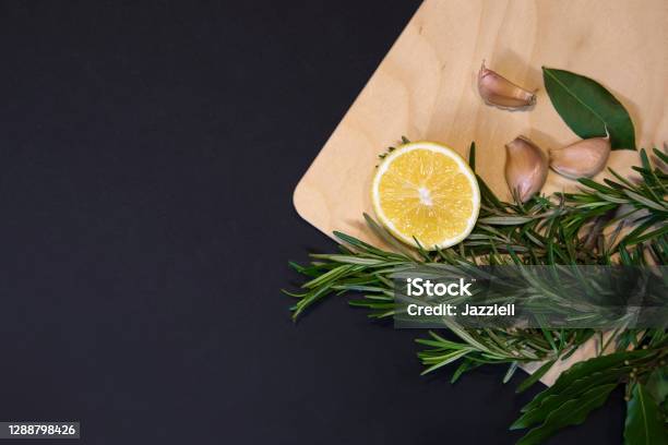 Cutting Board With Bay Leaves Rosemary Sprigs Lemon And Cloves Of Garlic Stock Photo - Download Image Now