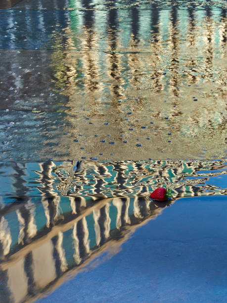 Surreal, colourful and fun image, taken around King's Cross, London. Image shows a reflection in a fountain, the reflection filling the whole frame and inverting the actual scene. The scene itself consists of a strawberry (possibly plastic?) in the fountain, framed so it appears in the window of the reflected building. The building itself appears to melt out of reality, as the reflection is broken by ripples in the water.