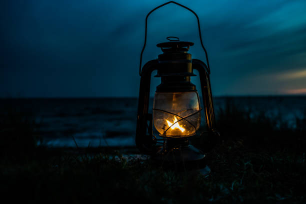 Old classic oil lantern burning with an orange flame by the ocean at dusk. Old classic oil lantern burning with an orange flame by the ocean at dusk. old oil lamp stock pictures, royalty-free photos & images