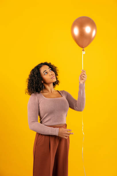 istock Thoughtful woman looking at balloon while standing against yellow background 1288802842