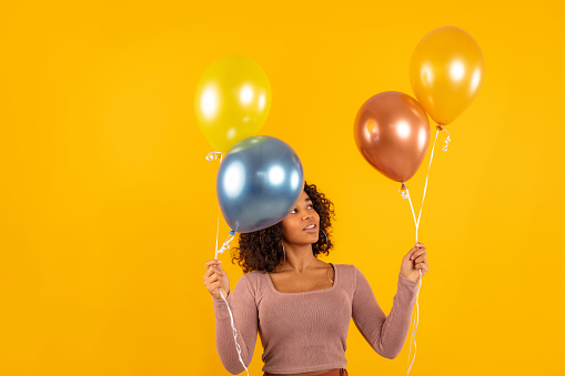 Young woman holding colorful balloons on yellow background