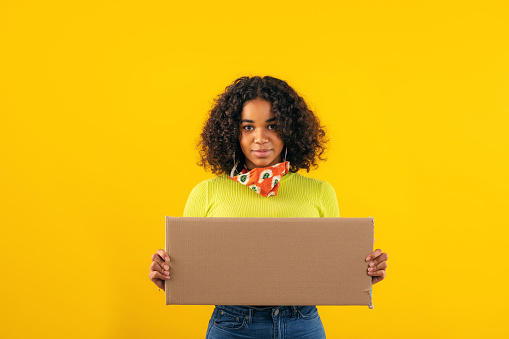 Beautiful young woman showing blank cardboard against orange background
