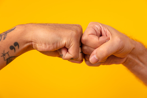 Hands Of male friends giving fist bump for greeting against yellow background