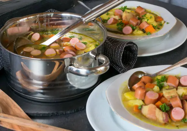 fresh and homemade cooked potato stew with hot dogs served on a table with plate, pot and ladle. Ready to eat