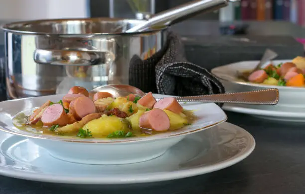 fresh and homemade cooked potato soup with sausages served on a table with plate and pot