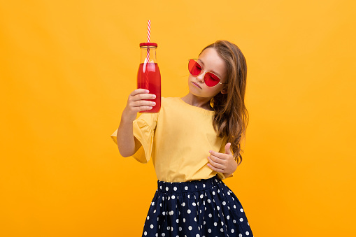 teenager girl with a glass of juice on an isolated yellow background with copy space.
