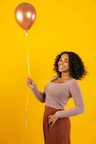 istock Cheerful young woman holding balloon while standing against yellow background 1288804474