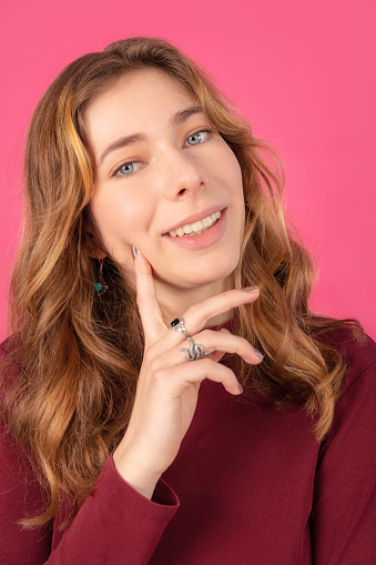 Close-up portrait of beautiful teenage girl with finger on cheek against pink background
