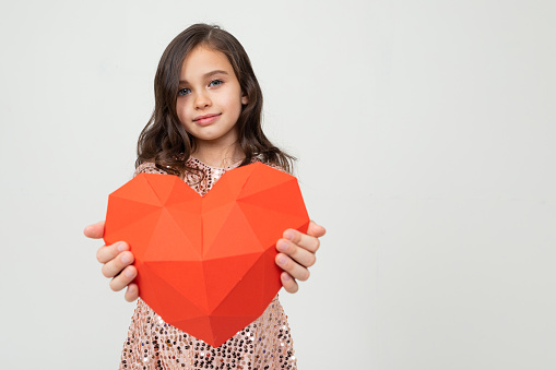 European young girl holding a heart-shaped figure in a studio with a light background and copy space.