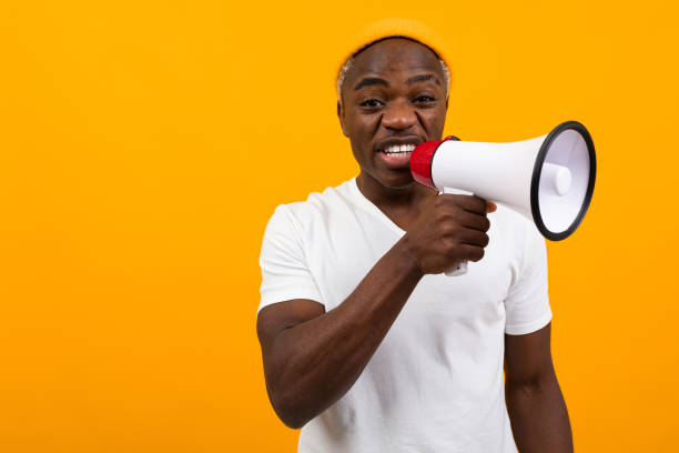 istock black african man shouts in a megaphone on a yellow background 1288805559