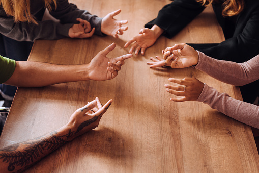 Cropped image of friends gesturing while discussing on wooden table in cafe