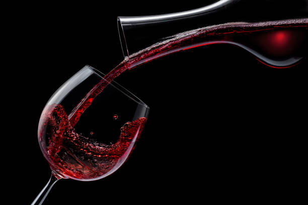 istock Red wine is poured into a wine glass on a black background. 1288805813