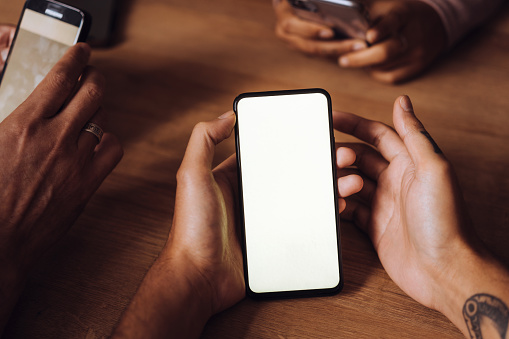 Hands of friends using mobile phones on table in restaurant at weekend