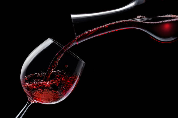 le vin rouge est versé dans un verre à vin sur un fond noir. - carafe decanter glass wine photos et images de collection