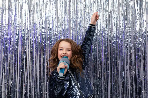 Photo of stylish girl singing with a microphone in her hands and a raised hand up on a shiny background