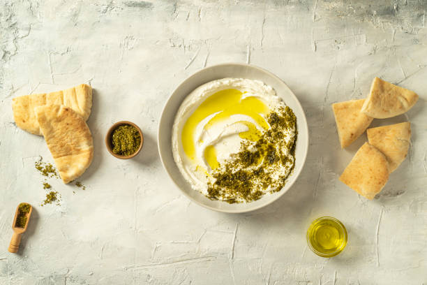 Popular middle eastern appetizer labneh or labaneh, soft white goat milk cheese with olive oil, hyssop or zaatar, served with pita bread on a grey table, top view, stock photo