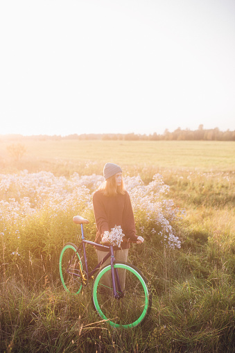 Young woman coming from meadow, holding wild flowers and her bicycle.