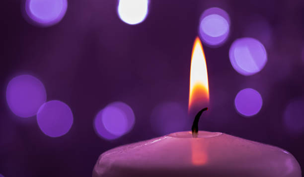istock Close up of one burning candle with blurred Christmas light background 1288809562