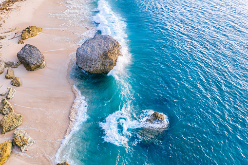 Bali, aerial shot of the turquoise ocean and beach full of big rocks.