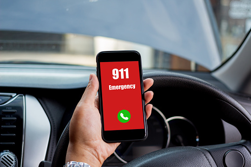 Hand holding cell phone with emergency number 911 in car