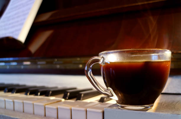 closeup uma xícara de café quente com fumaça no piano com folha de música borrada - piano sheet music old fashioned classical style - fotografias e filmes do acervo