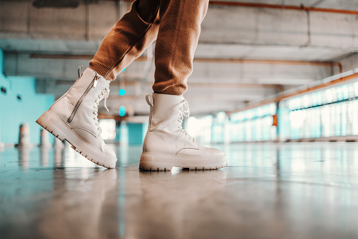 Cutout picture of fashionable woman walking in underground garage in whte boots.