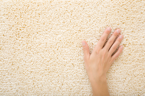 Young adult woman hand touching new beige shaggy carpet. Closeup. Choice of the best type and quality. Empty place for text. Top down view.
