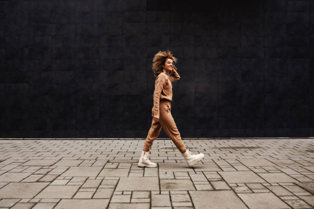 joven mujer de moda con el pelo rizado caminando en la calle y escuchando la música. - cosmopolitan fotografías e imágenes de stock