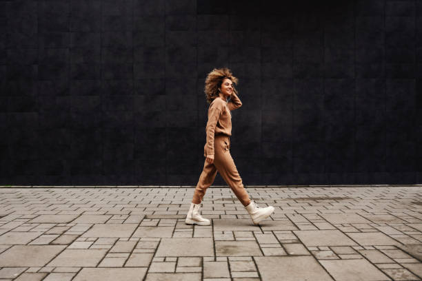 young fashionable woman with curly hair walking on the street and listening to the music. - fashion woman imagens e fotografias de stock