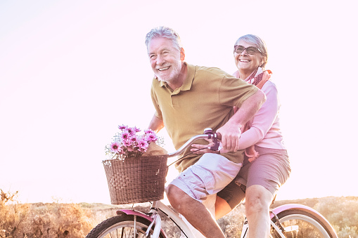 Cheerful mature couple of senior enjoy the outdoor leisure activity together riding a bike and laughing a lot - happy elderly active lifestyle with caucasian old people having fun