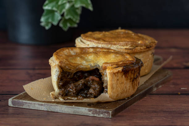Meat or beef pies on wooden board, wooden table and plant in background Meat or beef pies on wooden board, rustic timber table with dark black background savory food photos stock pictures, royalty-free photos & images