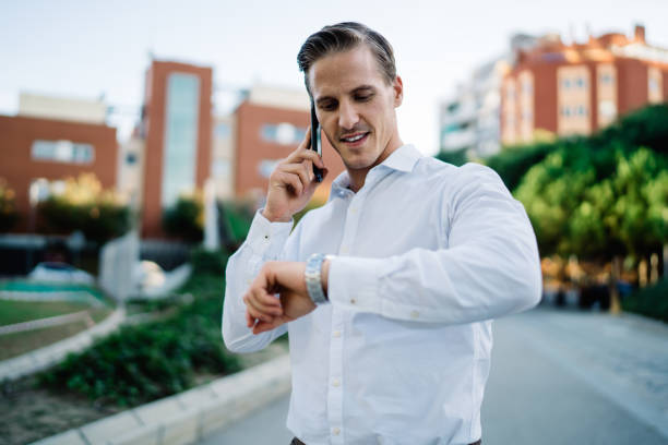 istock Positive man checking time on watch while answering phone call 1288831074