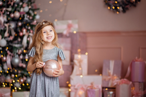Cute little laughing blonde girl with long hair plays with a Christmas ball on a background of Golden yellow bokeh . High quality photo